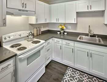 A kitchen with white cabinets and a white stove and sink